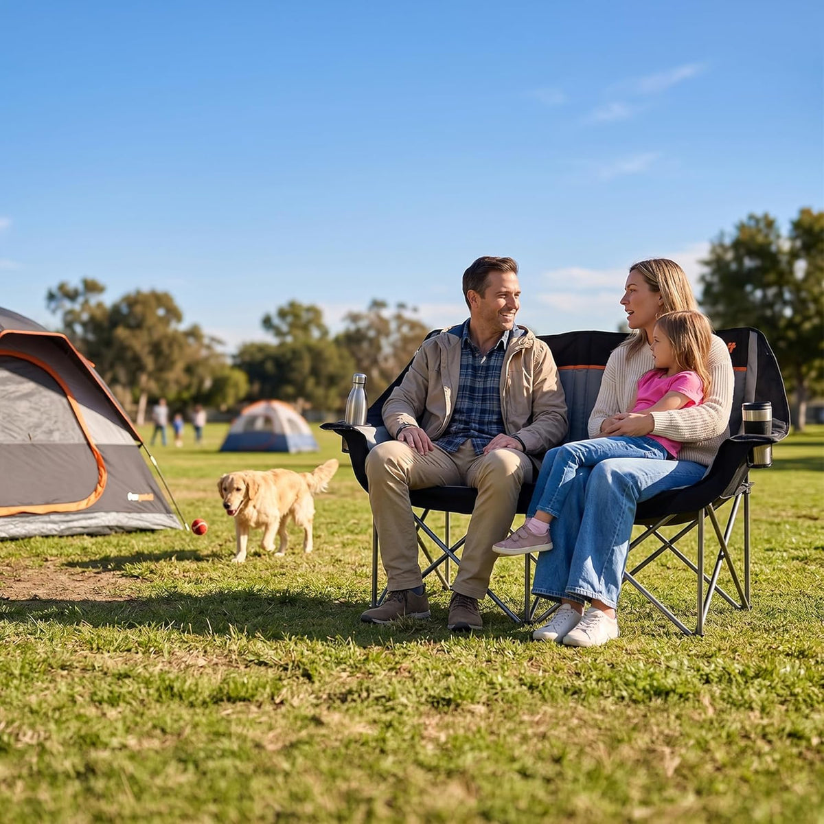 Couple and their dog sitting in a double folding camping chair at a campsite